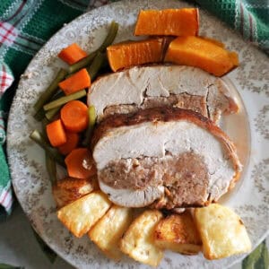 A plate with 2 slices of turkey breast stuffed with sausage meat, and roasted vegetables on the side.
