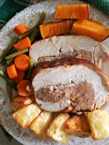 A plate with 2 slices of turkey breast stuffed with sausage meat, and roasted vegetables on the side.