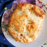 A white flowery plate with a whole baked brie wheel in puff pastry.