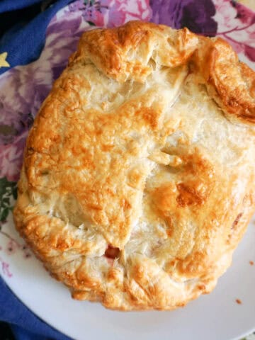 A white flowery plate with a whole baked brie wheel in puff pastry.