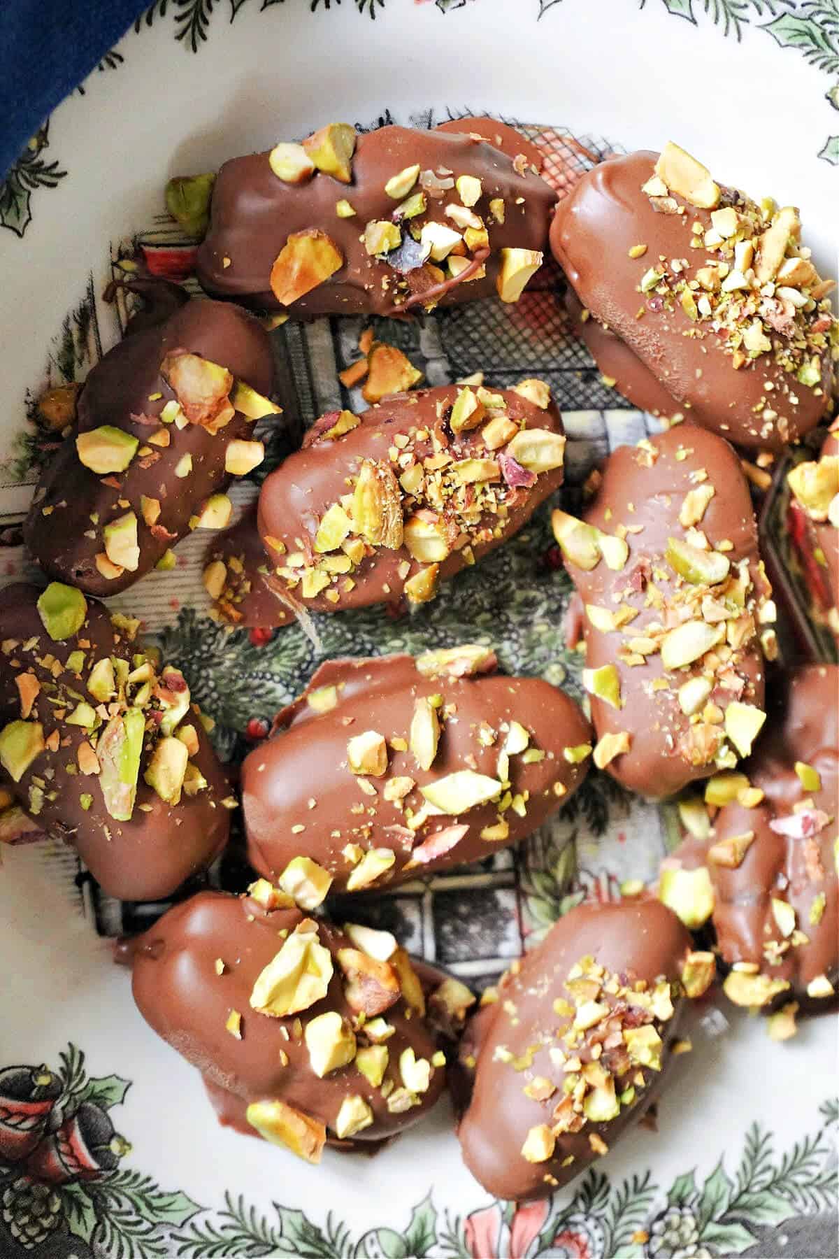 A plate with chocolate-covered dates garnished with chopped pistachios.