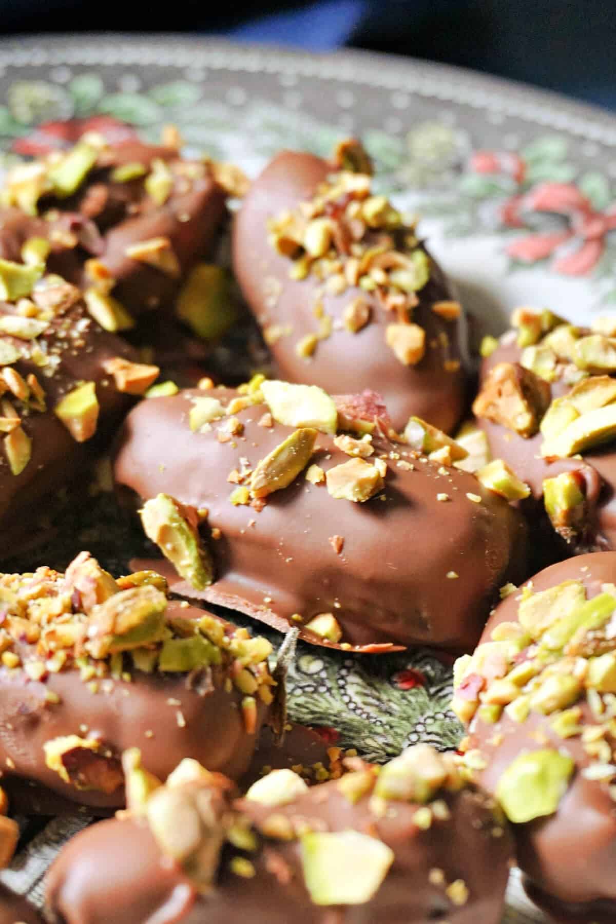 A festive plate with chocolate-covered dates garnished with chopped pistachios.