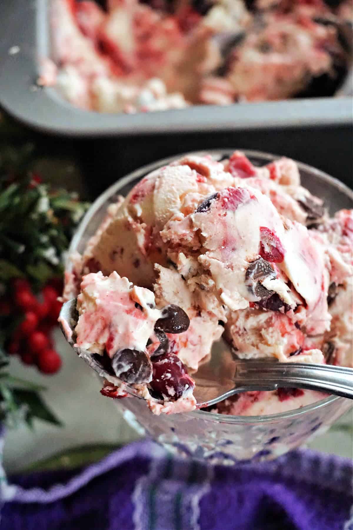 A dessert glass with red and white ice cream with chocolate chips and partially visible decorations and a tin with ice cream.