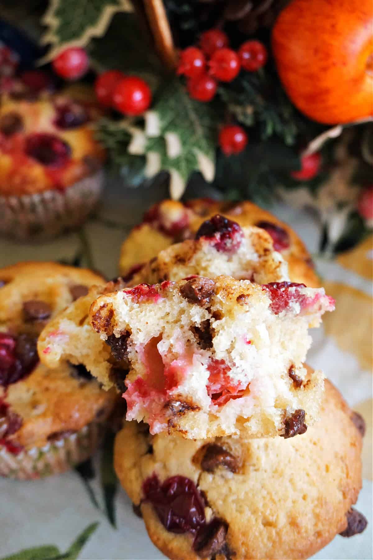 Half a cranberry choc chip muffin on top of 3 whole muffins. Christmas decorations around.