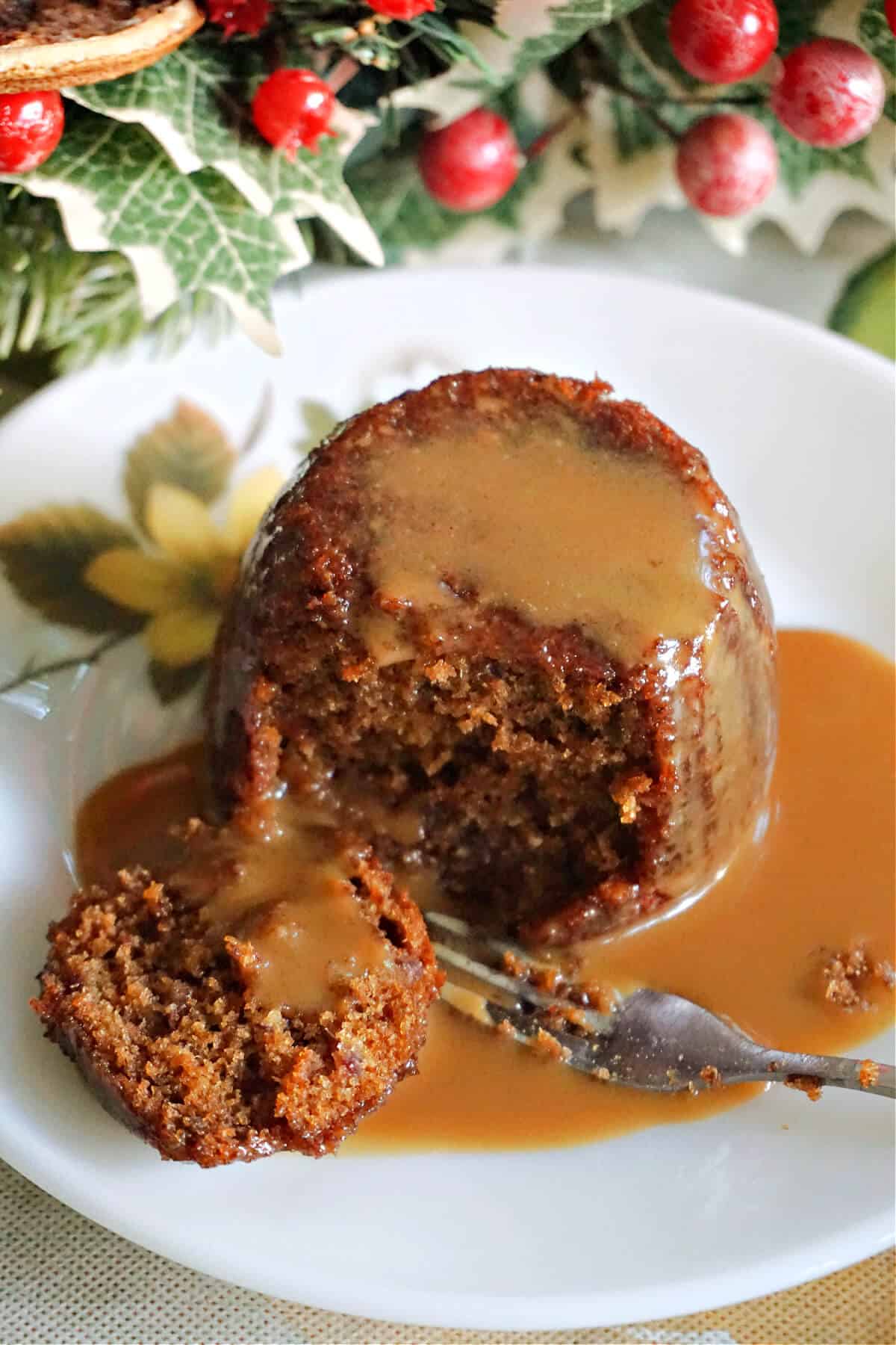 A plate with a mini sticky toffee pudding with toffee sauce and a fork cutting through it.