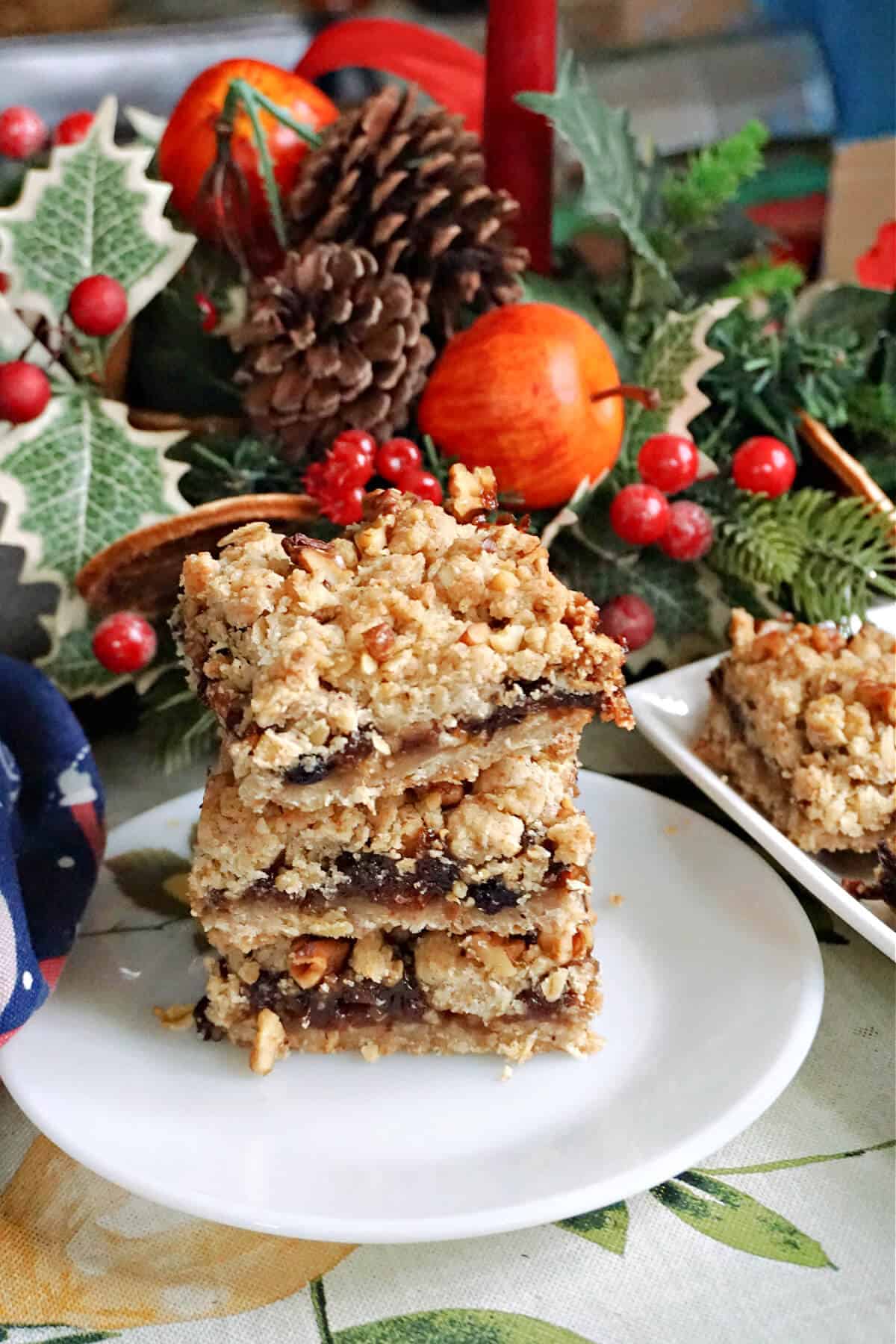 A white plate with a stack of 3 crumble bars and Christmas decorations around.