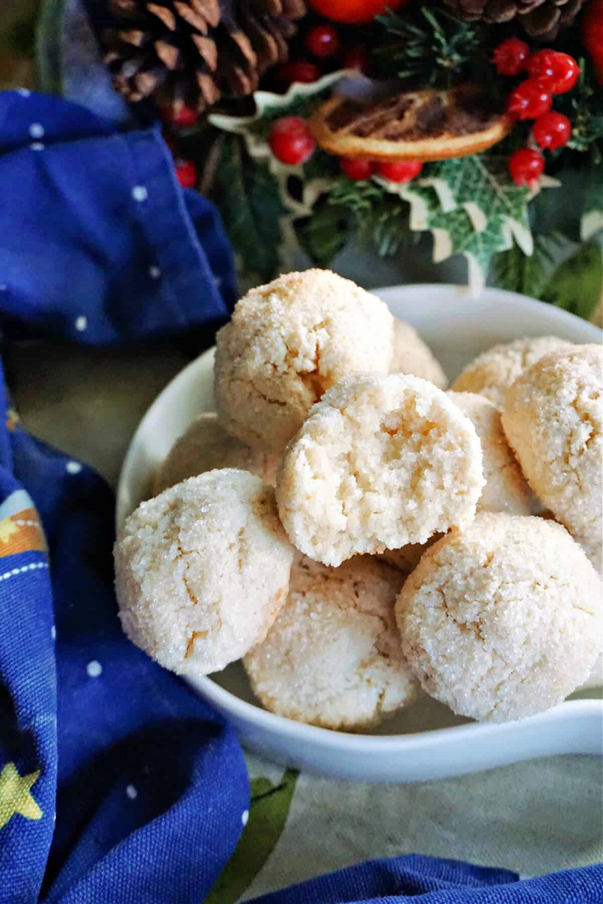 A white bowl with half an almond cookie sitting on top of other whole cookies and Christmas decorations around.