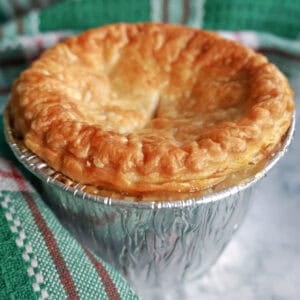 A foil case with a mini pie, green-patterned tea towel around.