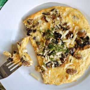 A white plate with a cheese and mushroom omelette and a fork resting on it.