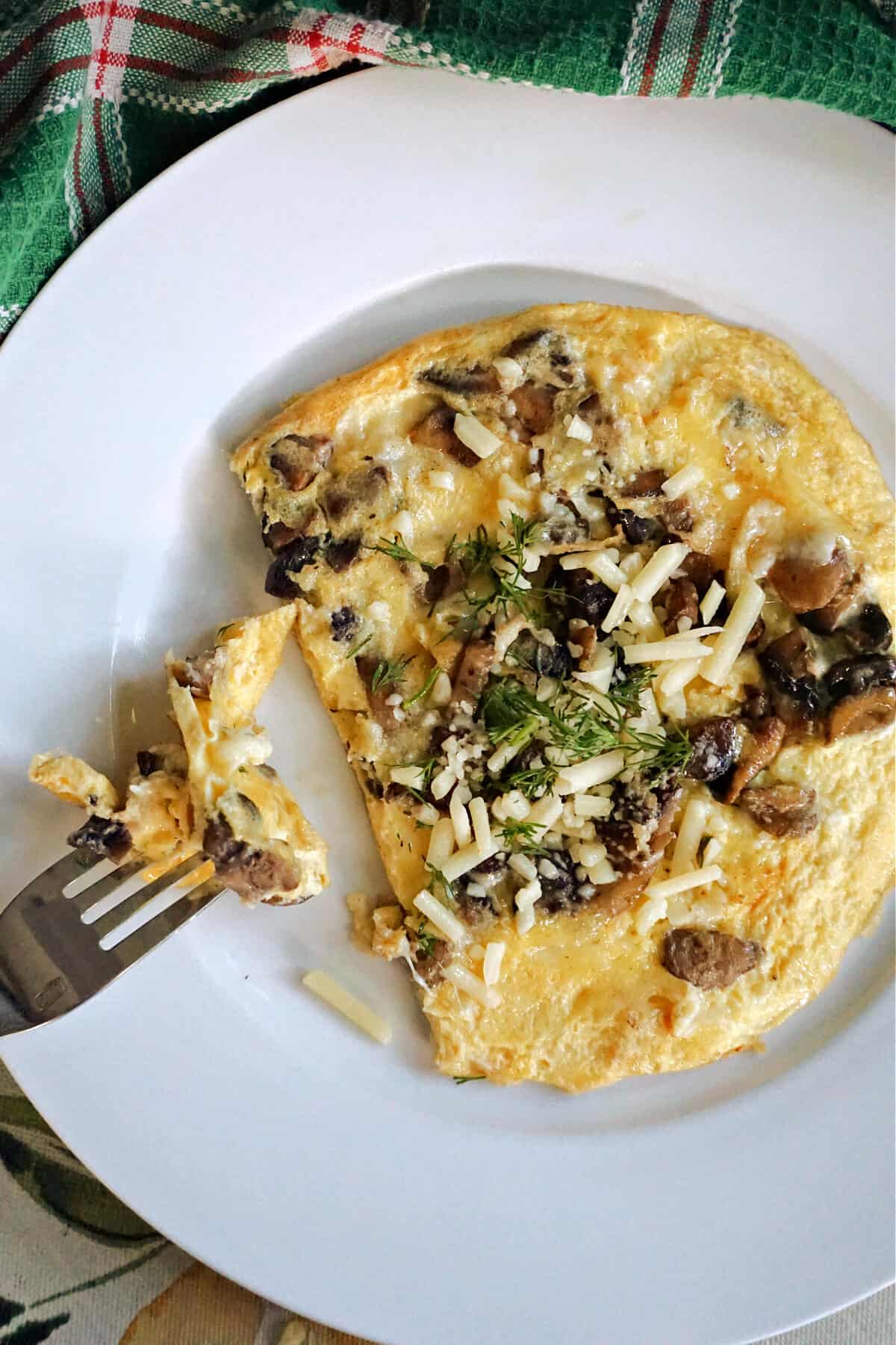 A white plate with a cheese and mushroom omelette and a fork resting on it.