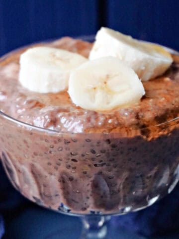 A glass with chocolate chia pudding topped with 3 slices of banana.