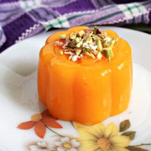 A white flowery plate with a mandarin jelly topped with chopped pistachios and grated chocolate.