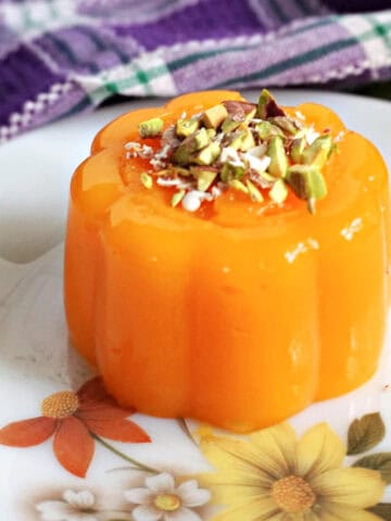 A white flowery plate with a mandarin jelly topped with chopped pistachios and grated chocolate.