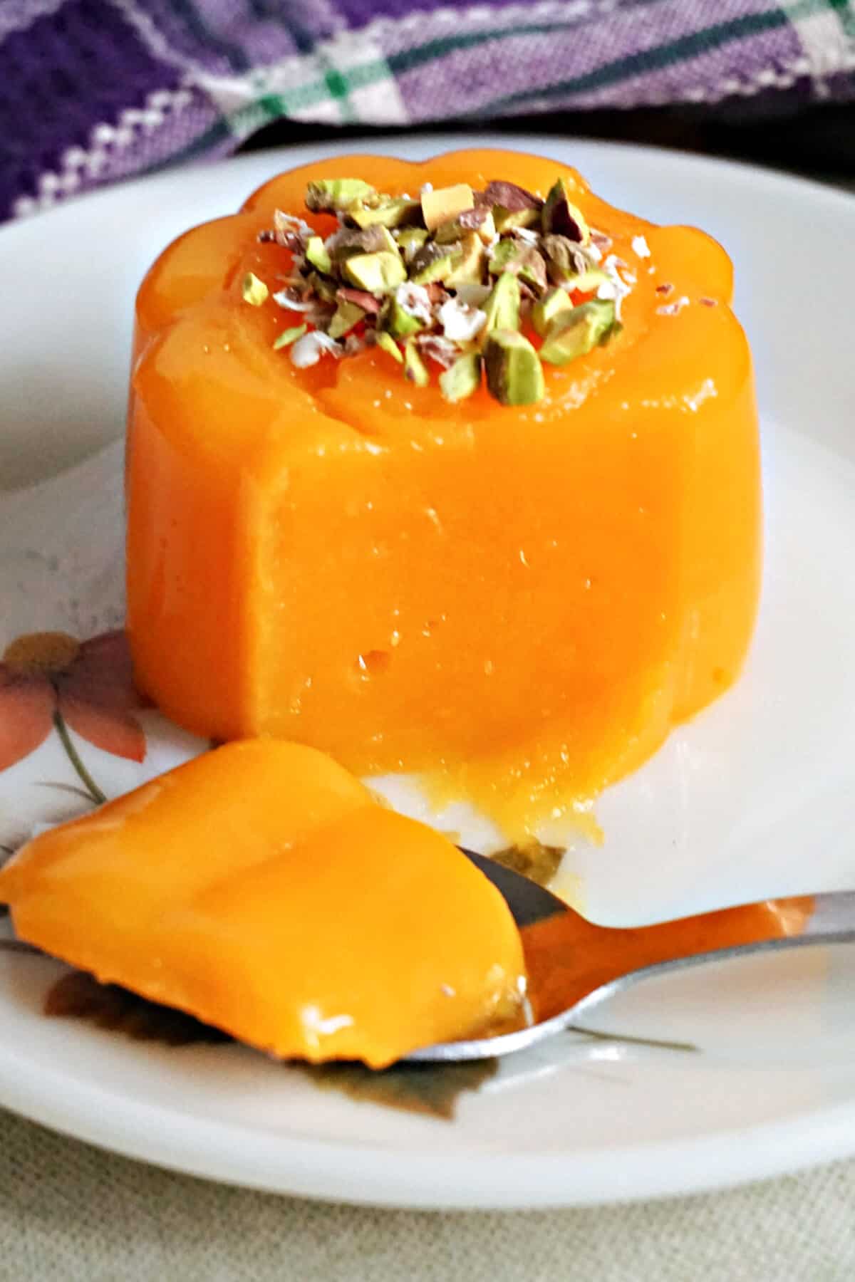 A flowery plate with a mandarin jelly and a dessertspoon of jelly sitting on the plate.