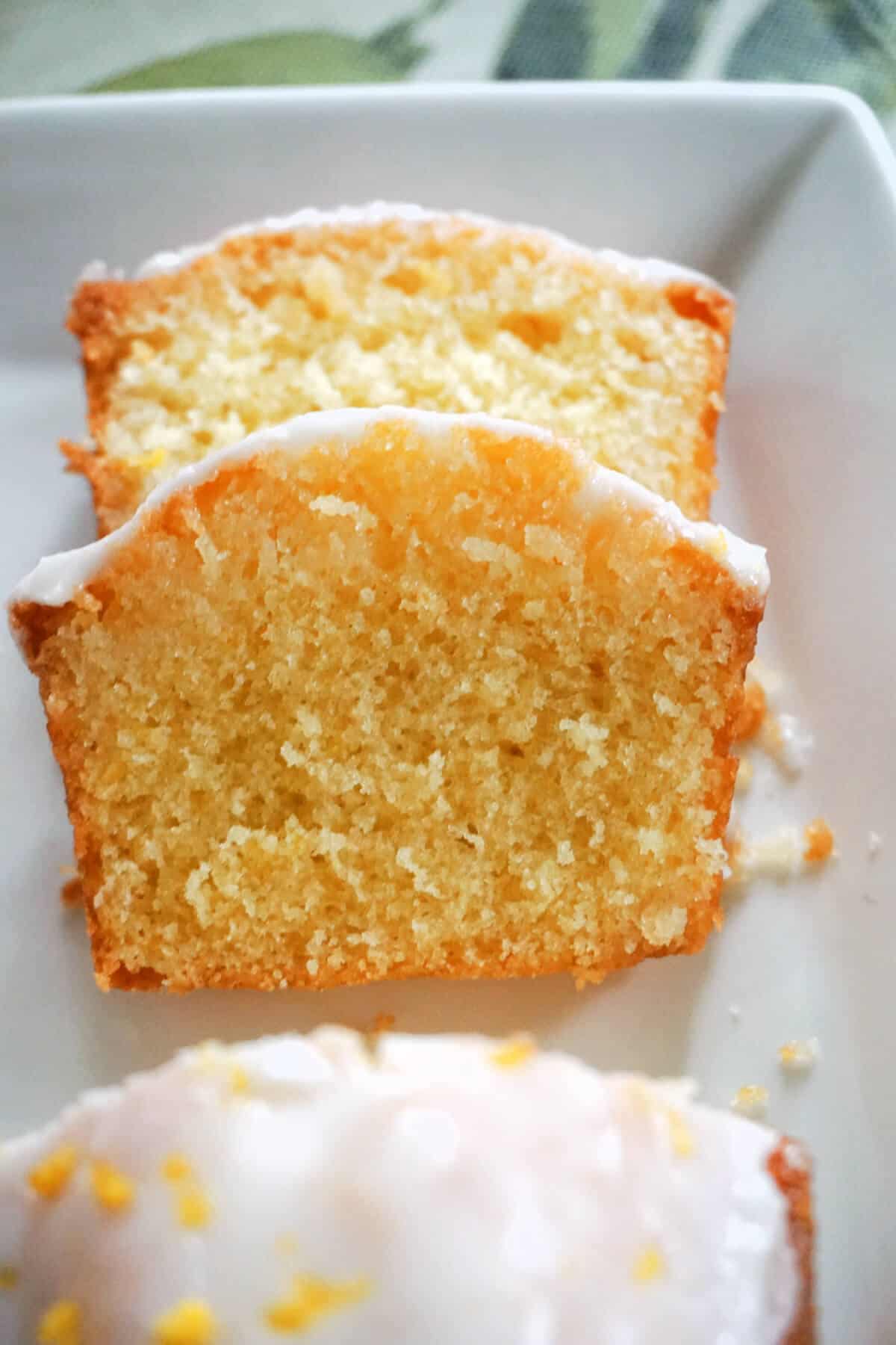 2 slices of lemon cakes on a white plate with a partially visible loaf cake.