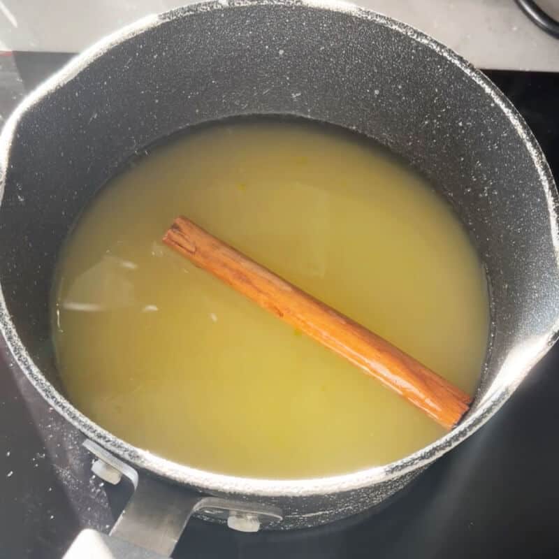 A pan with lemon syrup with a cinnamon stick in it.