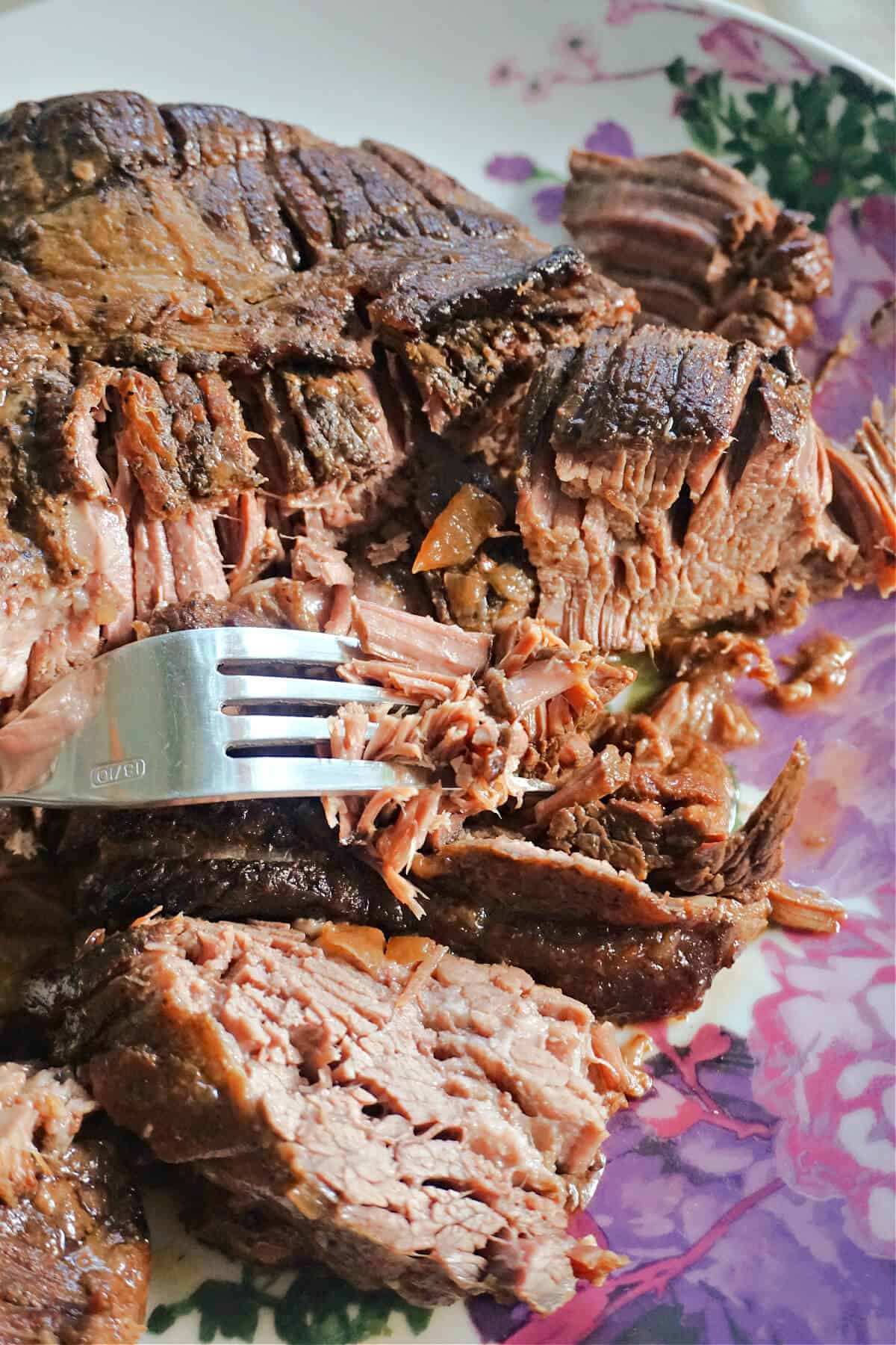 A flowery plate with shredded beef and a fork resting on it.
