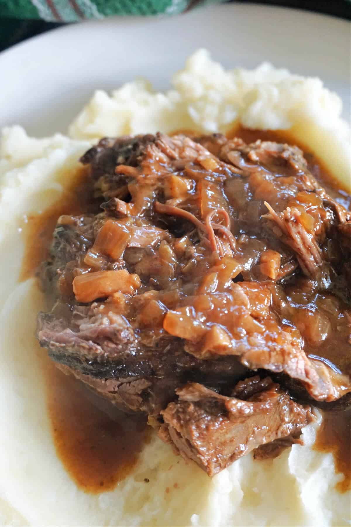 A white plate with shredded beef with gravy over a bed of mashed potatoes.