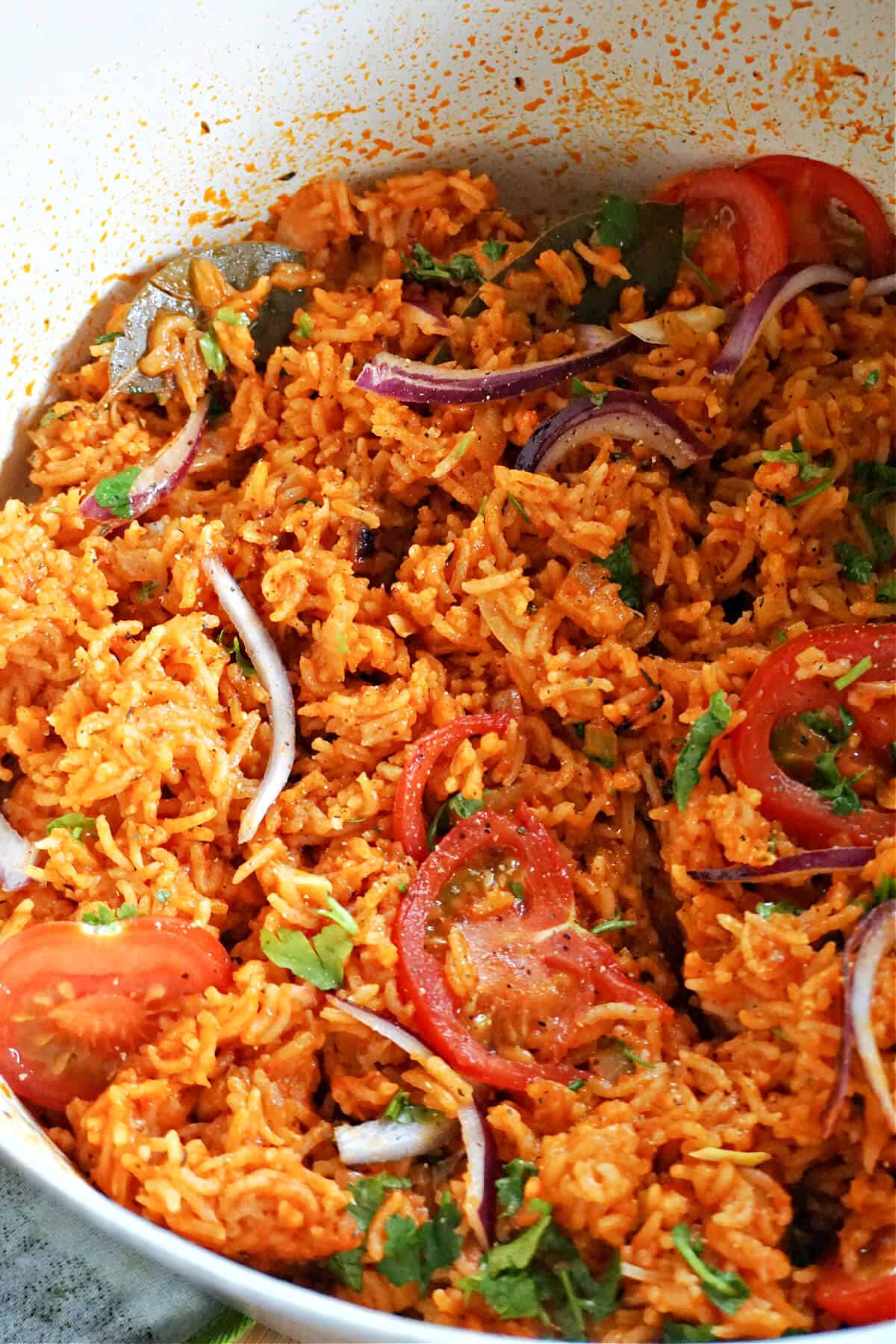 A pot with rice garnished with onion strips, tomato slices and parsley.