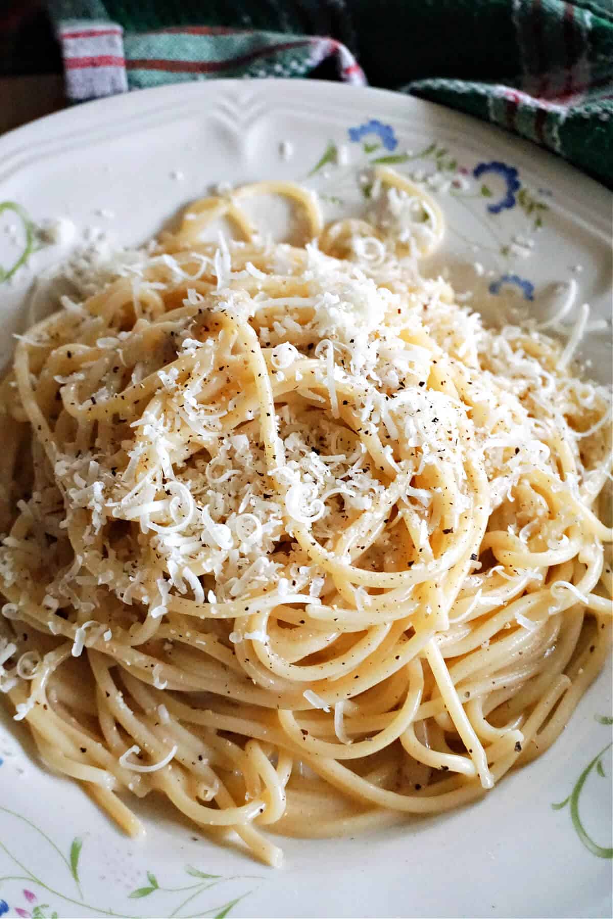 A white plate with a portion of cheese spaghetti garnished with ground black pepper.
