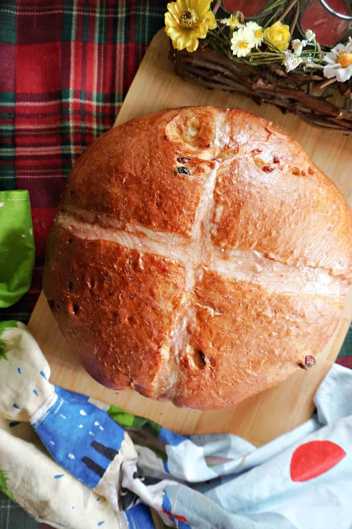 A hot cross bun loaf on a wooden board with a tea towel around.