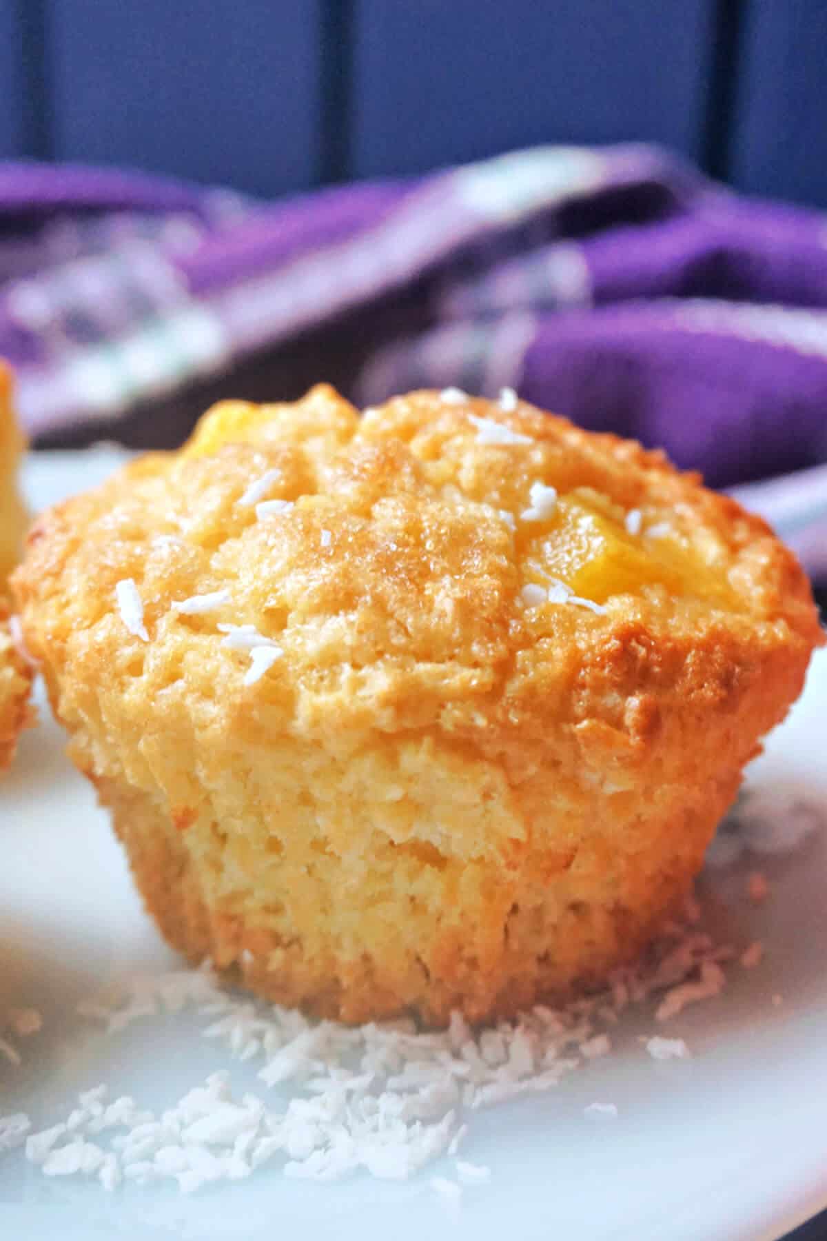 A muffin on a white plate with a purple-patterned tea towel in the background.