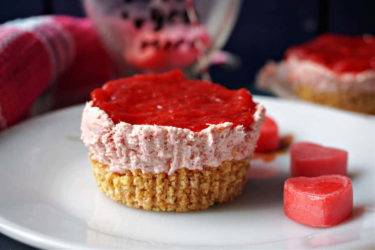 A white plate with an individual strawberry cheesecake and love hearts around.