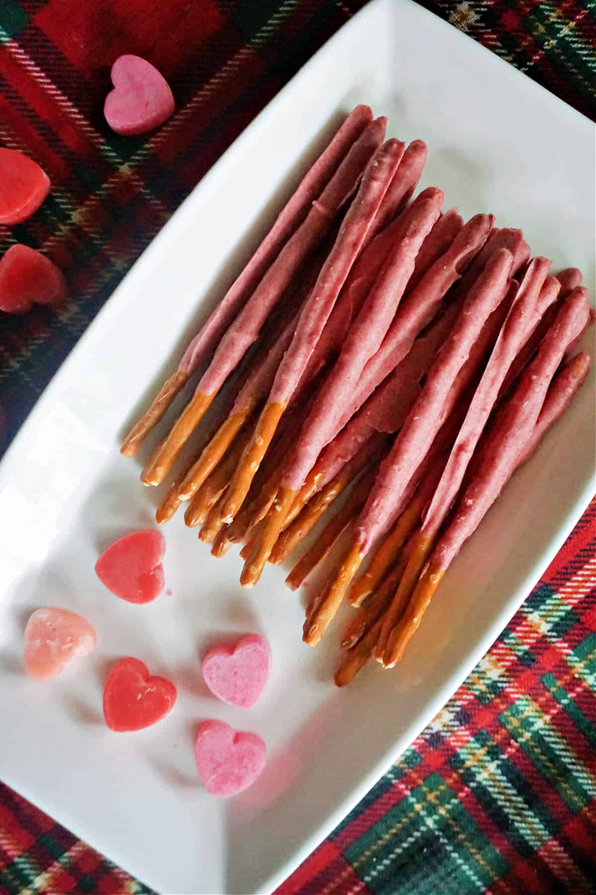 A white rectangle plate with pink chocolate-covered pretzel sticks and red and pink hearts around.