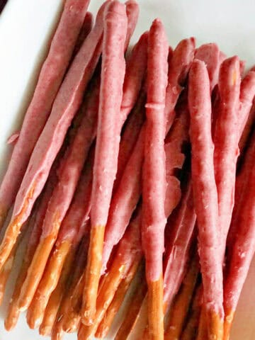 A white rectangle plate with pretzel sticks coated in pink chocolate.
