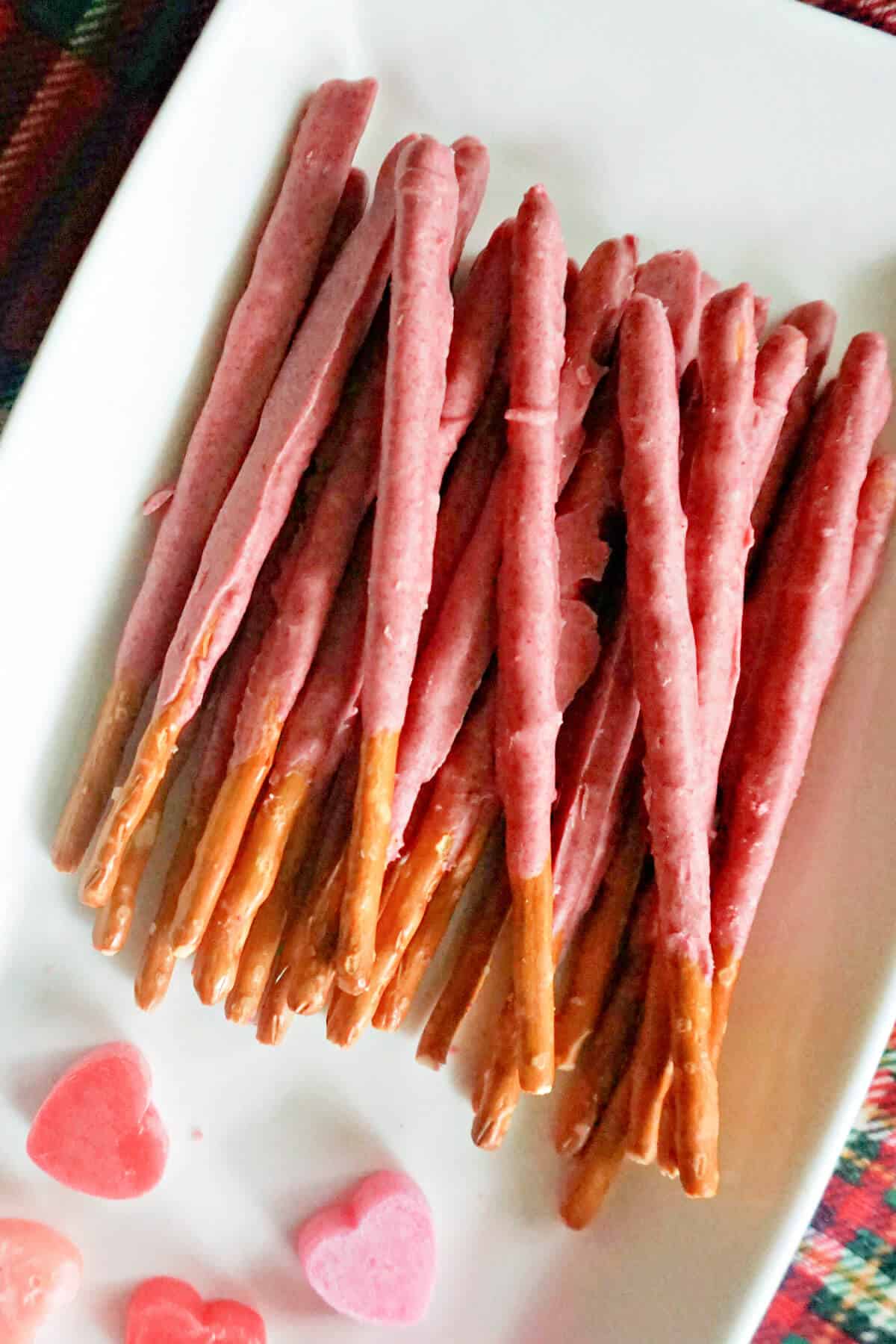A white rectangle plate with pretzels sticks covered in pink chocolate.