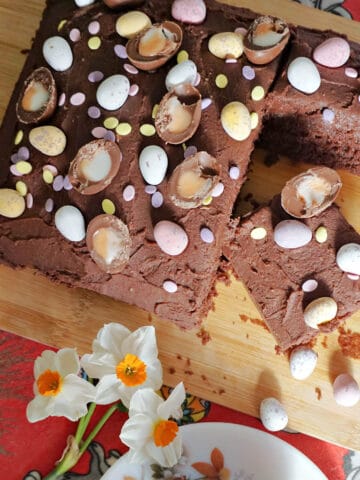 A wooden board with a sliced chocolate traybake cake decorated with Easter eggs.