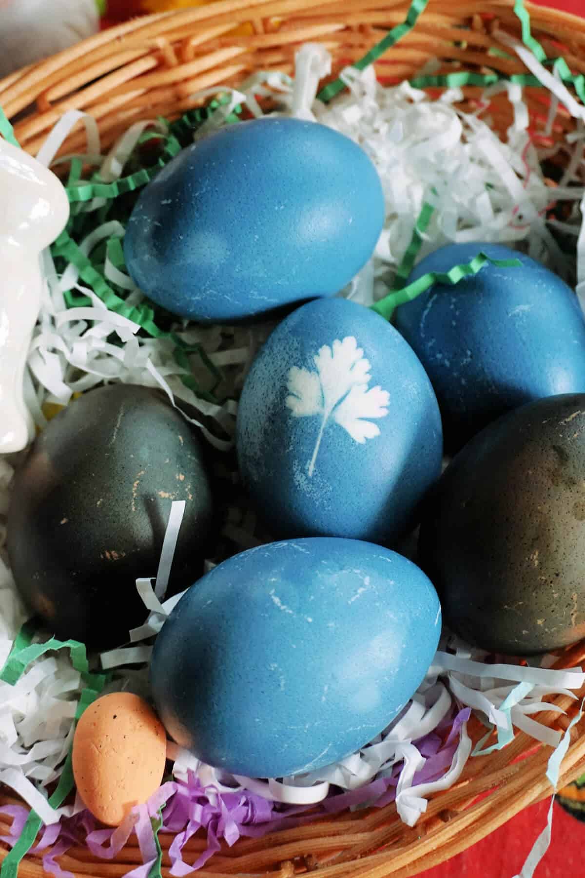 A basket with blue and dark green Easter eggs and Easter decorations around.