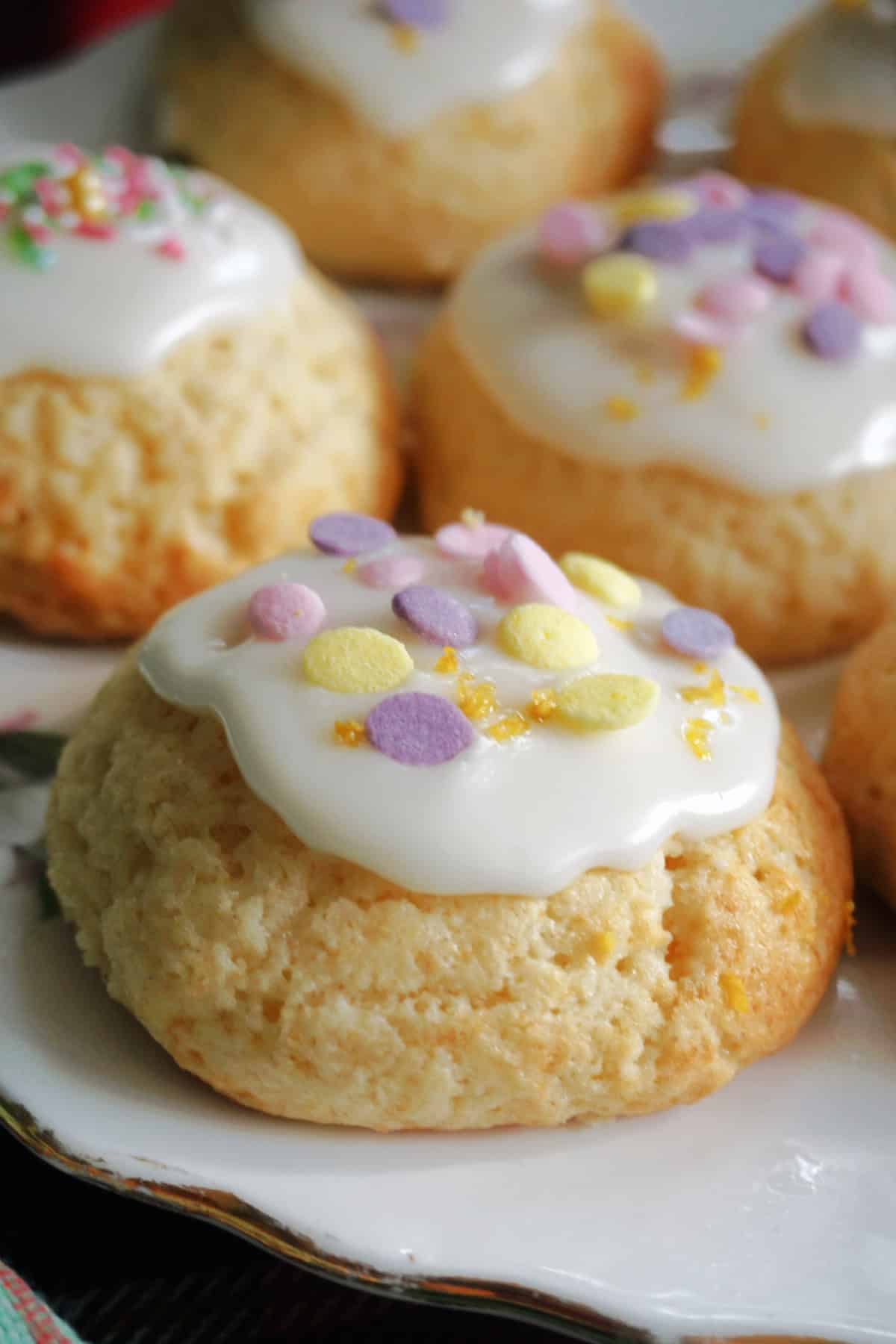 Close-up with lemon cookies topped with icing and Easter sprinkles on a white plate.