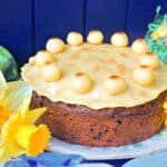 A simnel cake on a white flowery plate with Easter decor around.