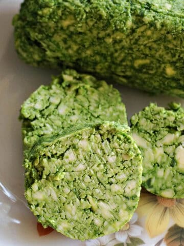 A white plate with 3 slices of wild garlic butter next to a long of wild garlic butter.