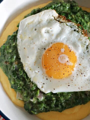 A white deep plate with creamy nettles with a fried egg over a bed of polenta.