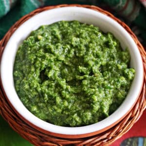 A white ramekin with pesto and a green-patterned tea towel around it.