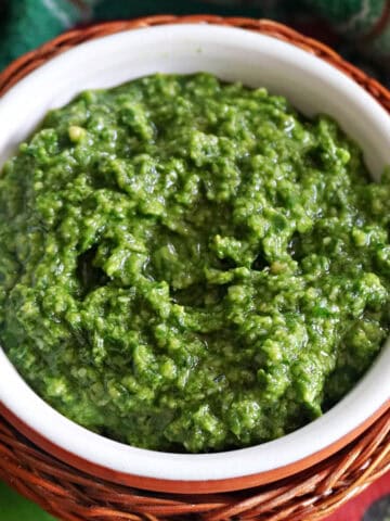 A white ramekin with pesto and a green-patterned tea towel around it.
