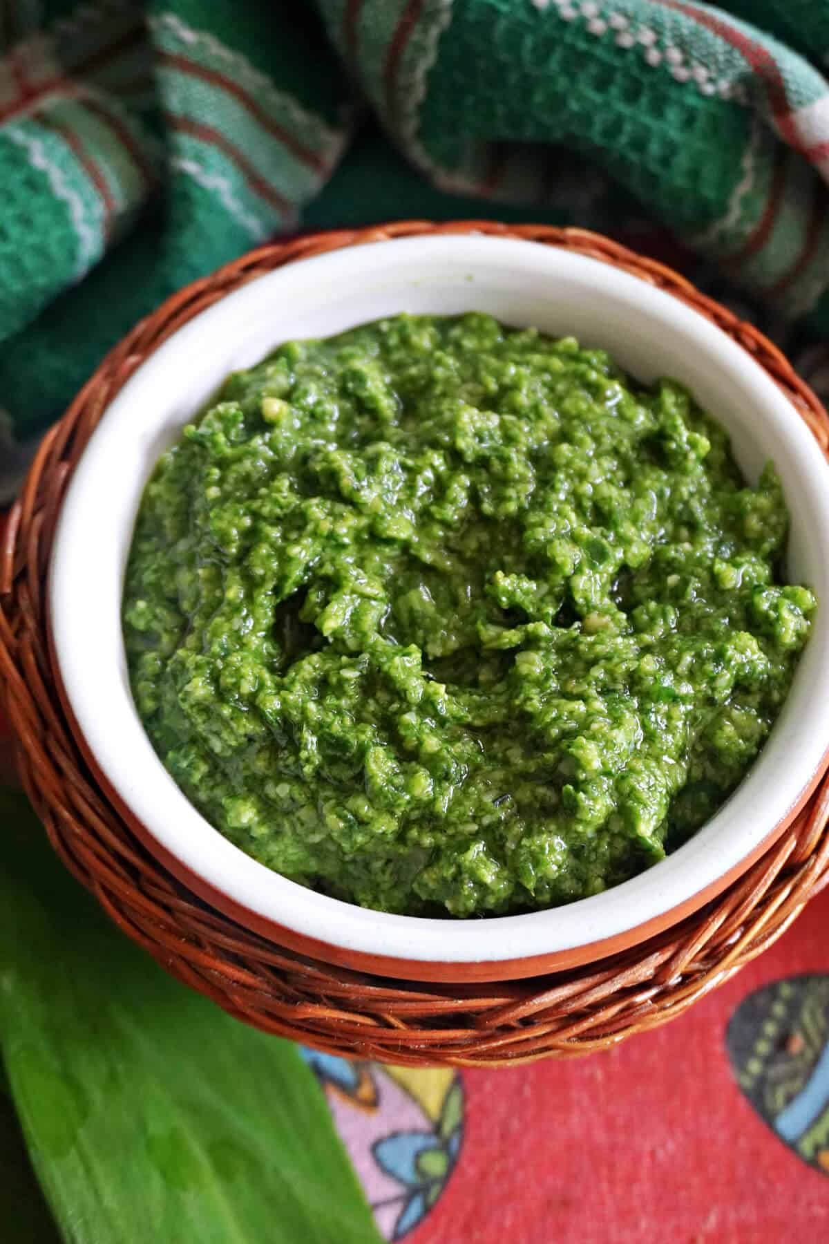 A white ramekin with pesto sauce with a green tea towel around.