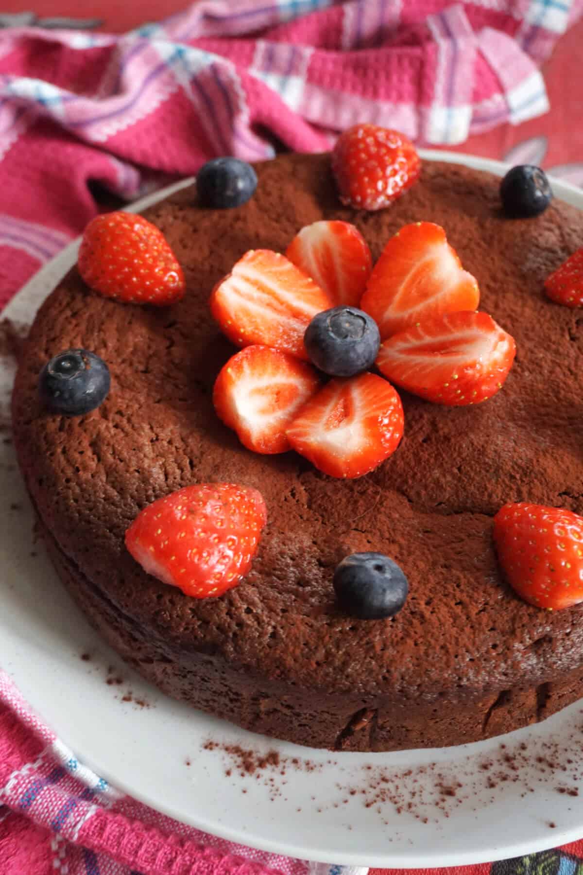 A white plate with a chocolate cake topped with strawberry slices and blueberries.