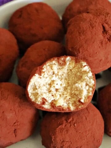 A white bowl with a half-eaten truffle sitting on top of other whole truffles.