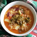 A white bowl with minestrone soup and a green-patterned towel around it.