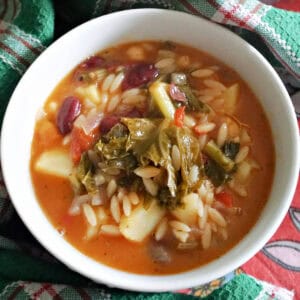 A white bowl with minestrone soup and a green-patterned towel around it.