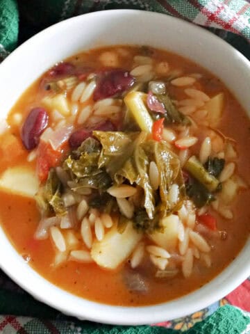A white bowl with minestrone soup and a green-patterned towel around it.