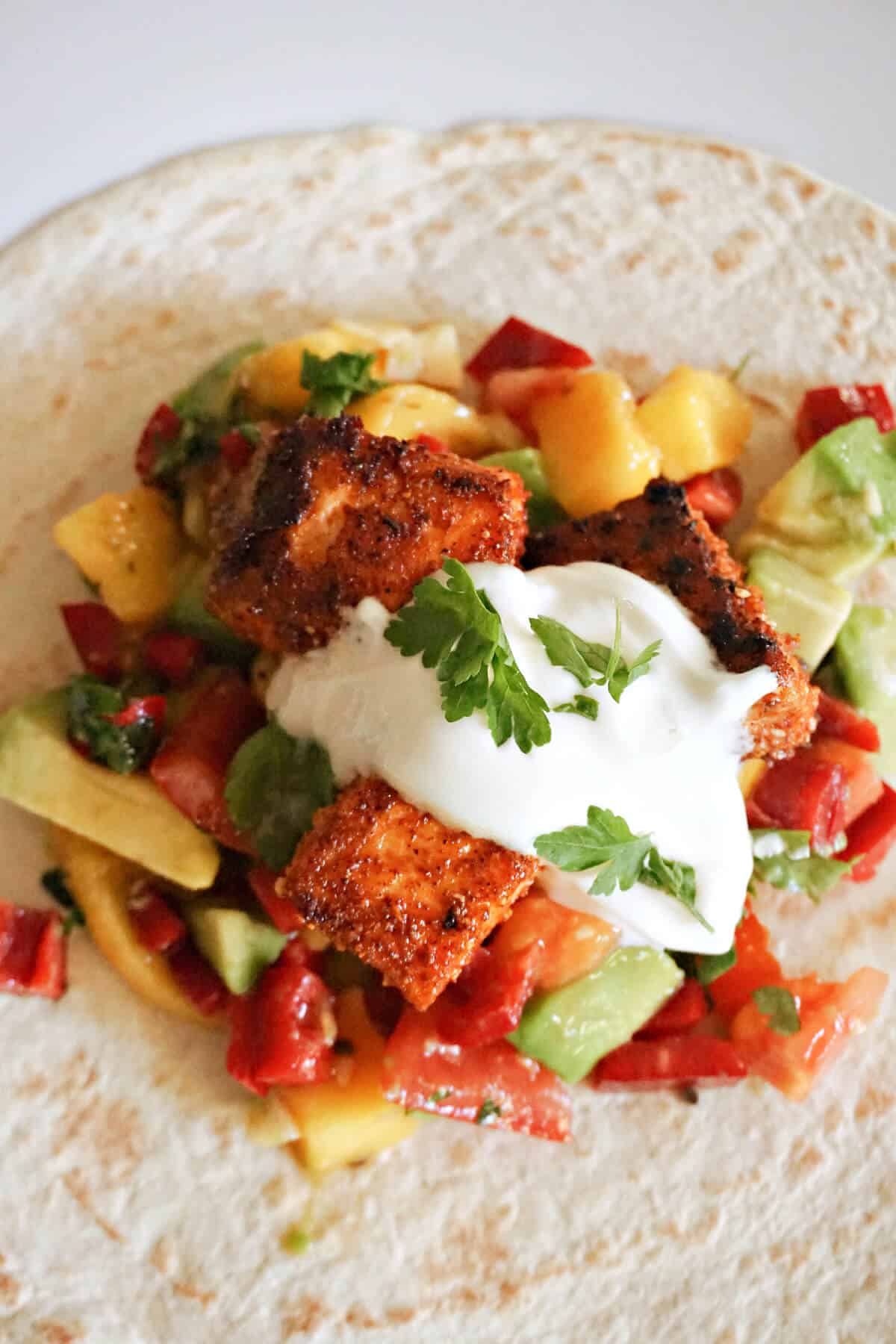 A tortilla wrap topped with salsa, salmon bites, sour cream and parsley leaves.