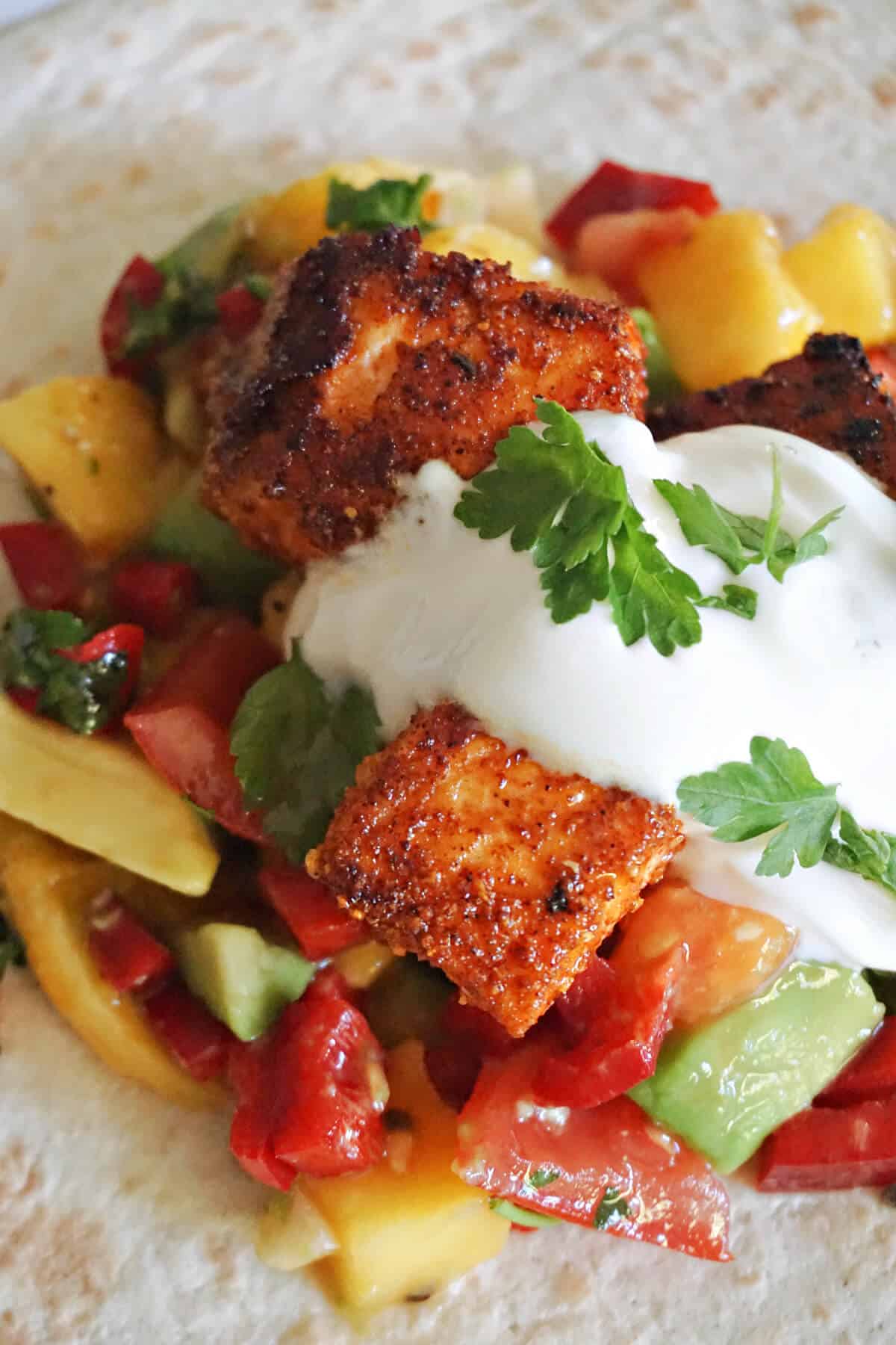 Close-up of a taco with salsa with salmon bites, sour cream and parsley leaves.