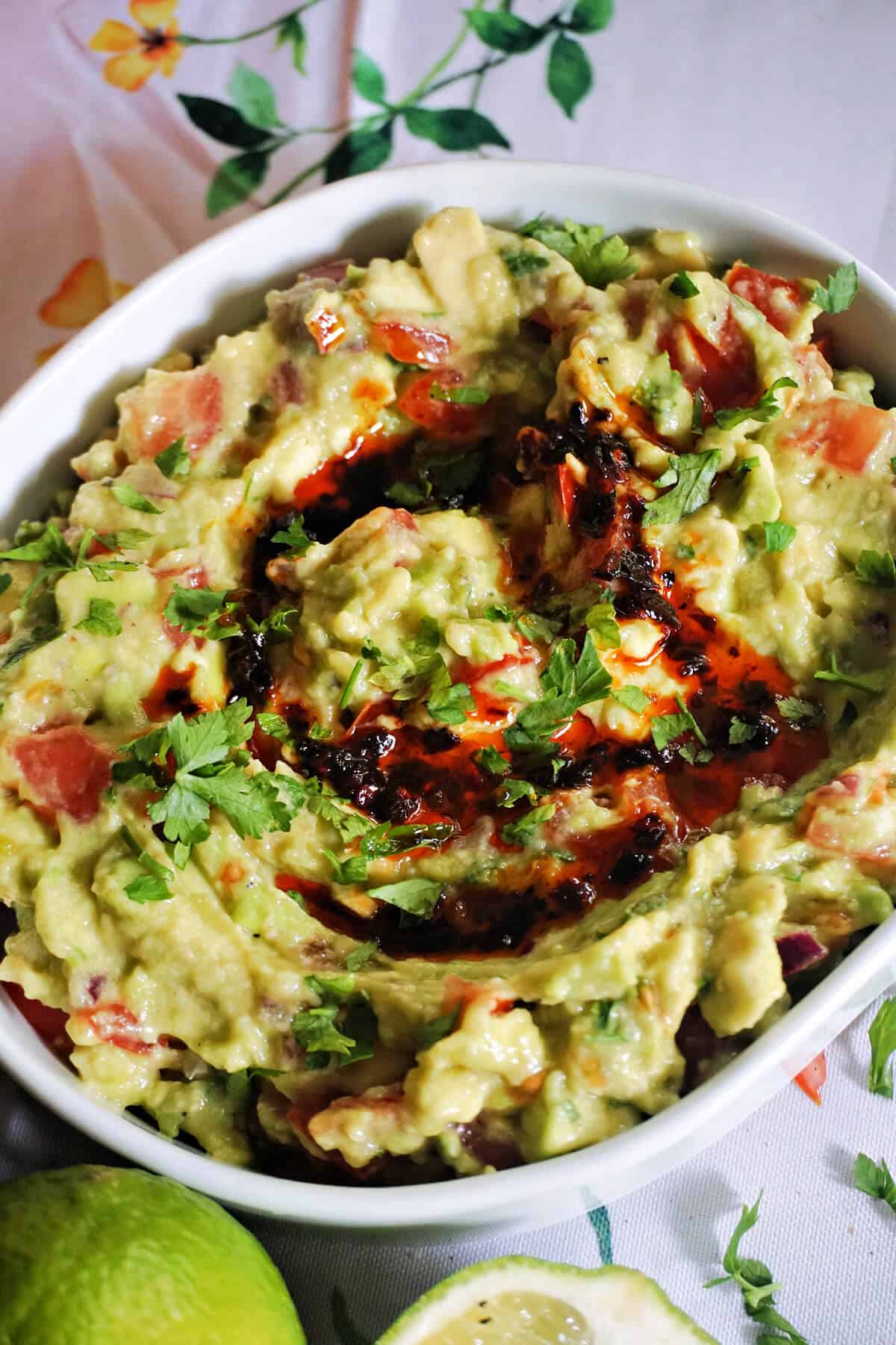 A white serving bowl with guacamole drizzled with chilli oil and garnished with chopped parsley.