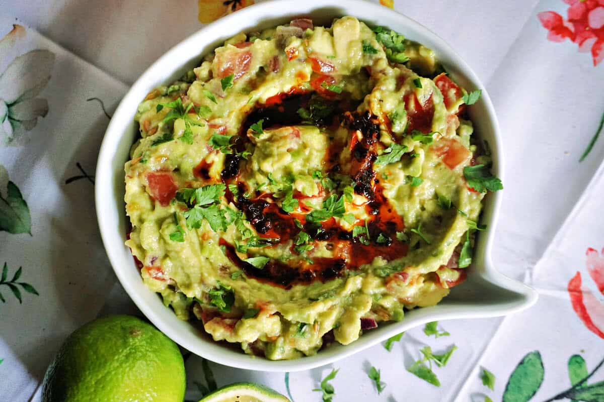 A white serving bowl with guacamole, partially visible whole lime and half a lime next to it.