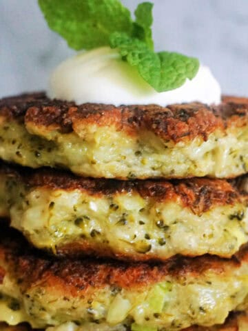 A stack of 4 broccoli fritters topped with yogurt and fresh mint leaves.