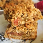 2 slices of rhubarb crumble bars piled up on a white plate.